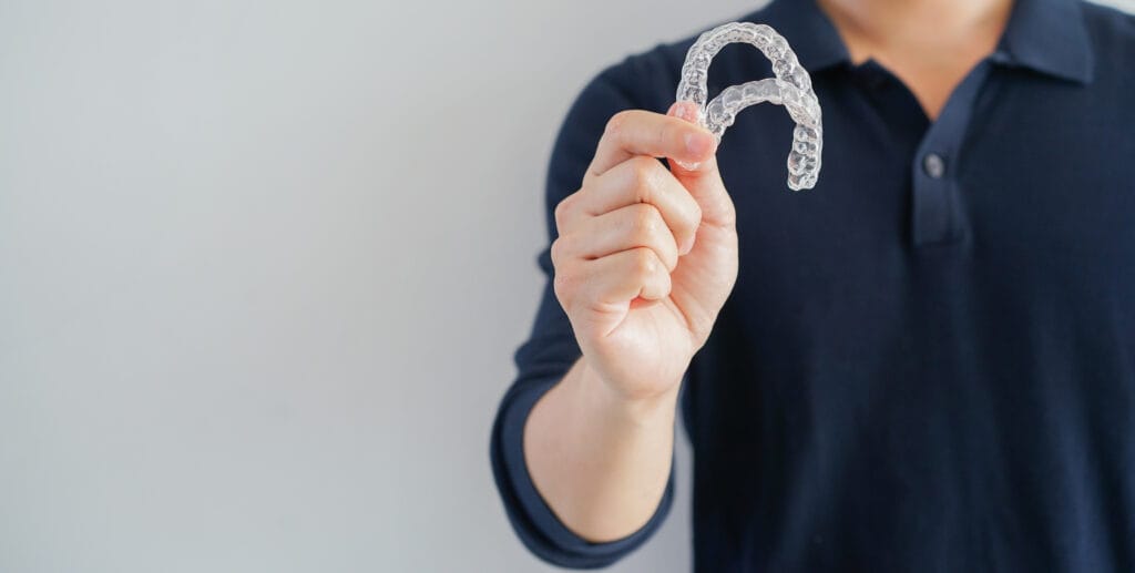 1 close up man hand holding to show dental aligner retainer tool (invisible) isolated on gray color background